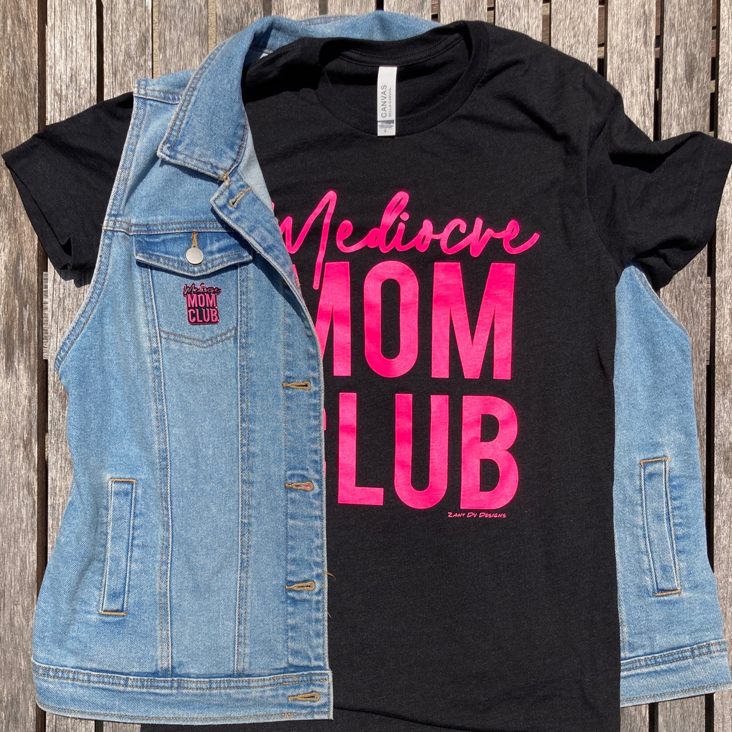 Mom club neon pink on black stacked tee with the writing in neon pink saying, "Mediocre MOM CLUB"