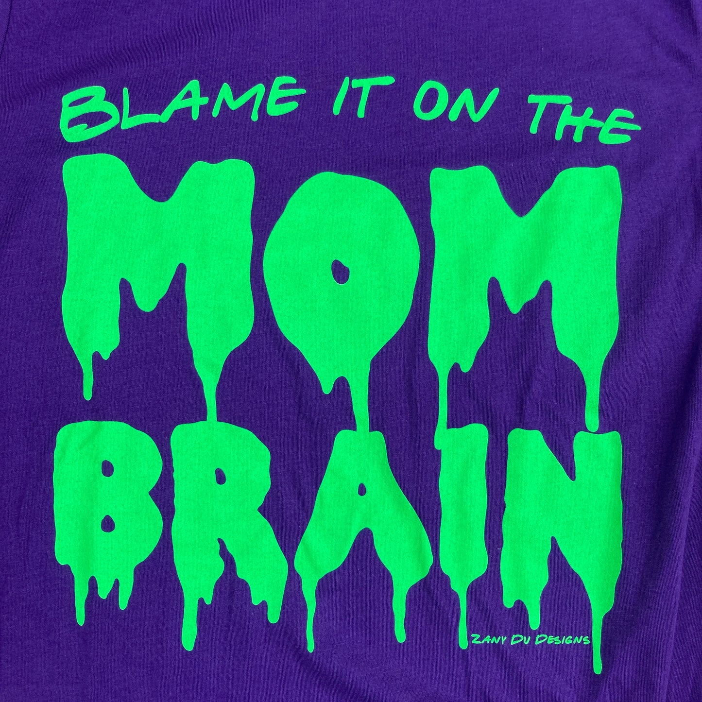 Slime purple and neon green tee with the writing saying, "BLAME IT ON THE MOM BRAIN" and the MOM BRAIN part has a slime font - Brain - Spooky - Halloween