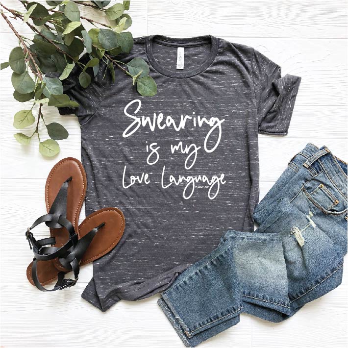 Grey heathered tee that says, "Swearing is my love language" in white script font laid with black sandals, denim and eucalyptus- sailor's mouth, bad words, cursing, cussing, mothehood