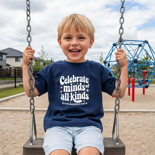 Child on a swing wearing a navy blue t-shirt with a message that reads "celebrate minds of all kinds" at a playground.