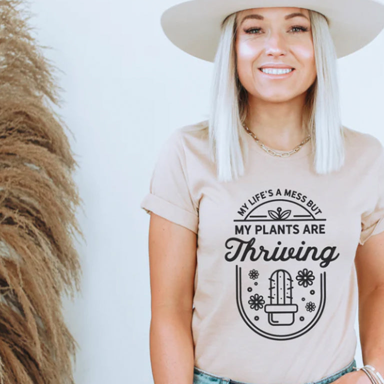 Woman wearing a beige t-shirt with a cactus design and text, standing against a plain background.