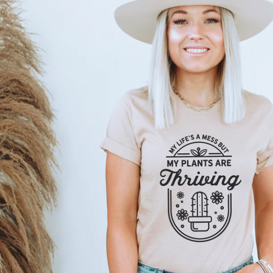 Woman wearing a beige t-shirt with a cactus design and text, standing against a plain background.
