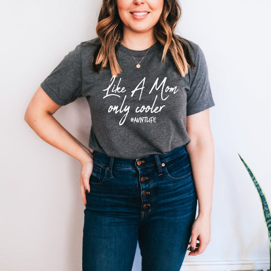 Person wearing a gray t-shirt with text that says like a mom only cooler #auntlife and blue jeans against a white background