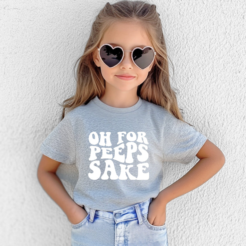 Child wearing a gray t-shirt with 'OH FOR PEEPS SAKE' text and heart-shaped sunglasses against a white background.