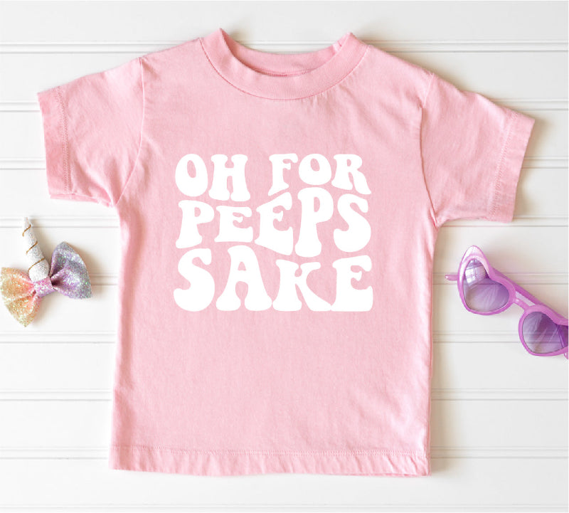 Pink t-shirt with 'OH FOR PEEPS SAKE' text on a white wooden surface.