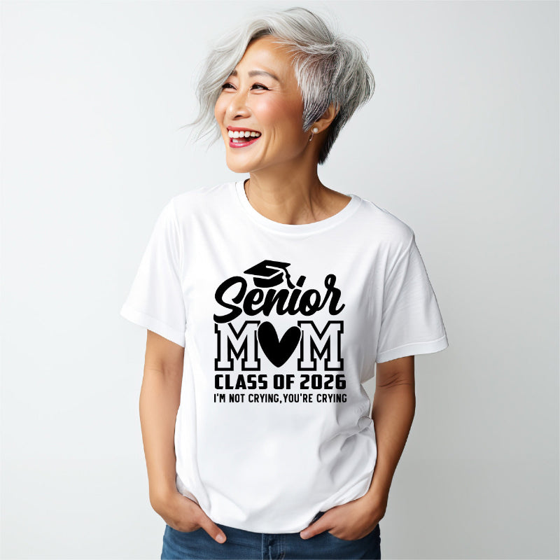 Woman wearing a white t-shirt with 'Senior Mom Class of 2026 I'm Not Crying, You're Crying' text on a plain background