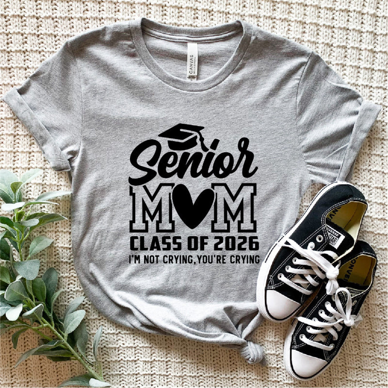 Gray t-shirt with 'Senior Mom Class of 2026' text and black sneakers on a textured surface.