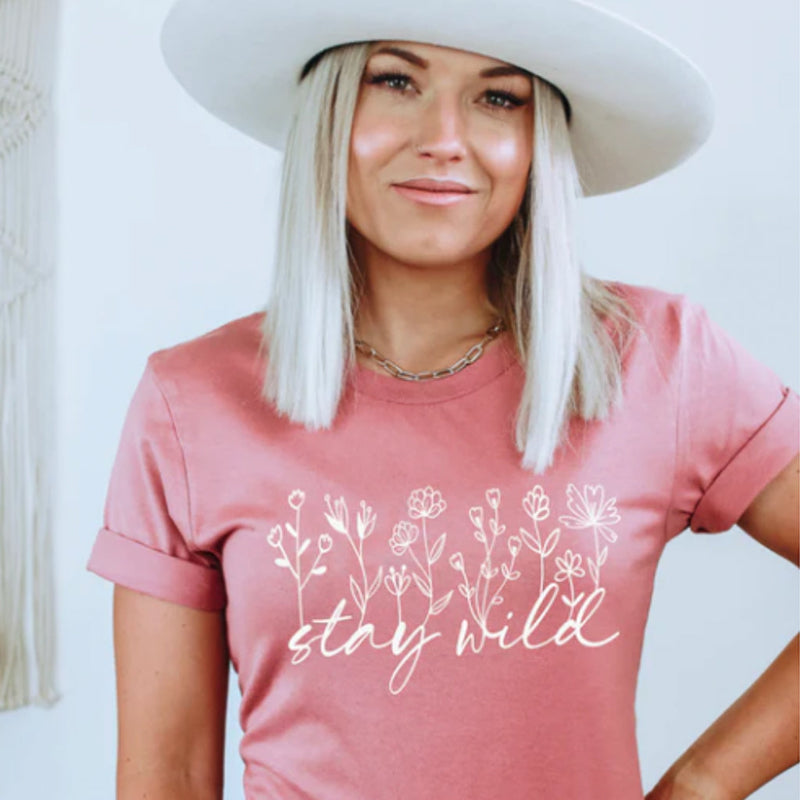 Woman wearing a pink t-shirt with floral design and 'stay wild' text.